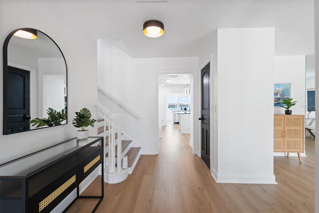 A bright entryway features light wood flooring, a staircase, a black console table, and arched mirrors — 900 79TH STREET S, ST PETERSBURG, FL