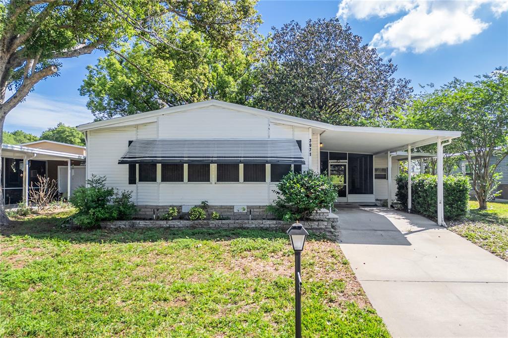 A single-story white house features a front carport, a screened porch, and a metal awning — 3971 COHEN DRIVE UNIT 739, ZELLWOOD, FL