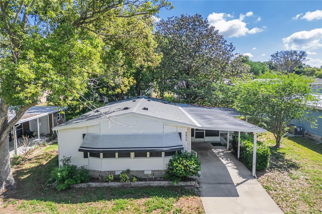 An exterior view of a single-story home with a carport, metal awning, and mature trees — 3971 COHEN DRIVE UNIT 739, ZELLWOOD, FL