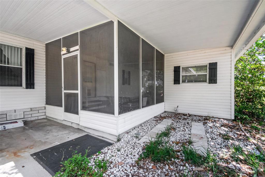 A white-sided home features a screened-in porch, a concrete patio, and a gravel yard — 3971 COHEN DRIVE UNIT 739, ZELLWOOD, FL