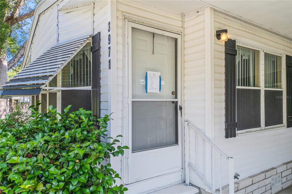 The exterior of a white house features a front door, a window with shutters, and landscaping — 3971 COHEN DRIVE UNIT 739, ZELLWOOD, FL