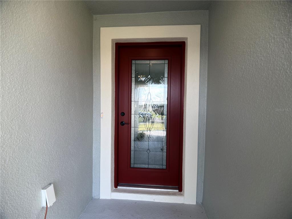 A red front door with a glass insert is set within a light-colored entryway — 3147 NE 45TH AVENUE, OCALA, FL