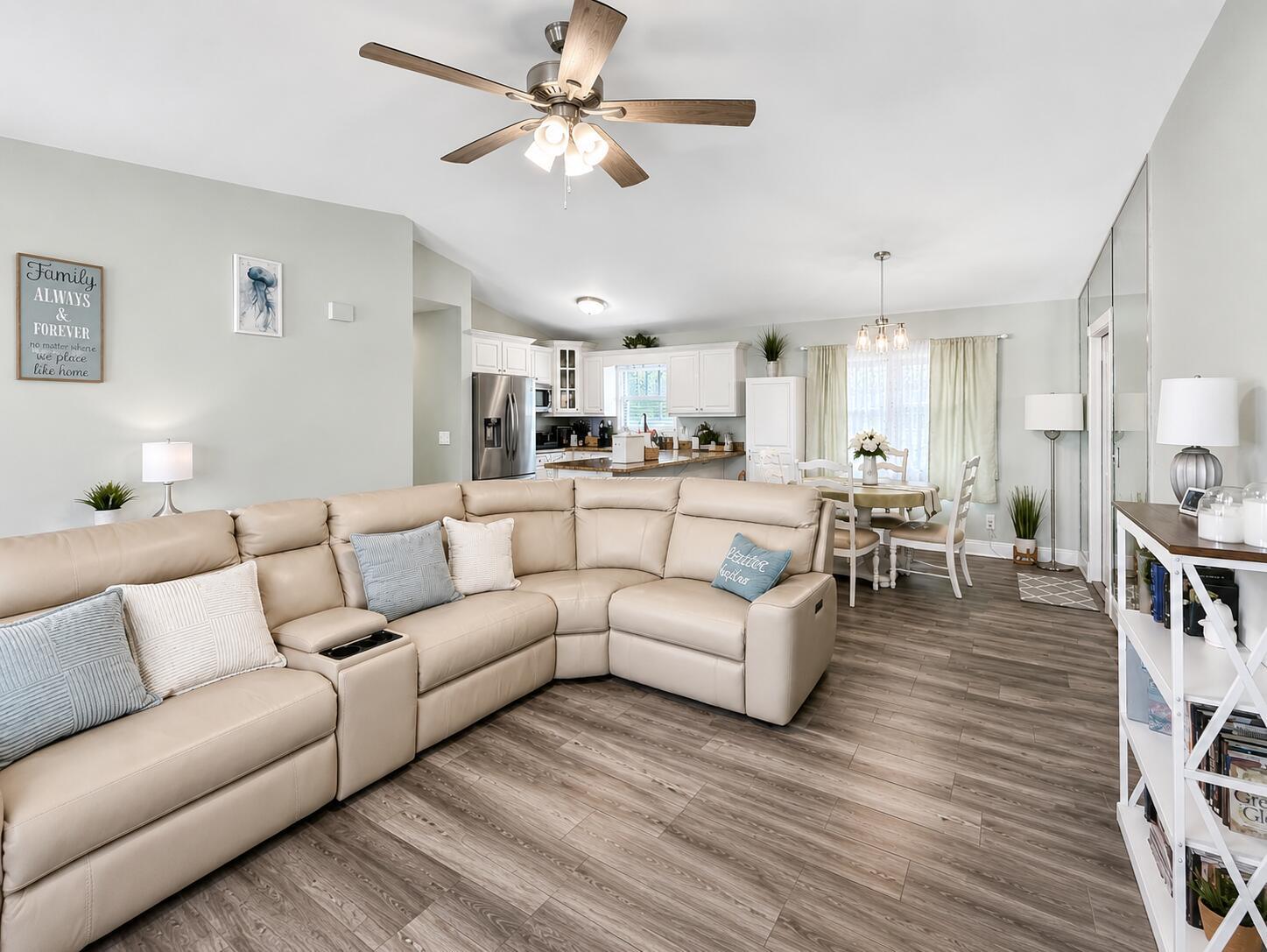 An open-concept living and dining area features a large beige sectional, wood-look flooring, and kitchen — 4436 SE Beckett Avenue, Stuart FL 34997, STUART, FL