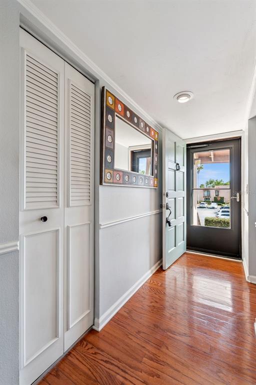 An entryway features hardwood floors, a louvered closet, a decorative mirror, and an open door — 210 LA CASA UNIT 210, LAKE WALES, FL