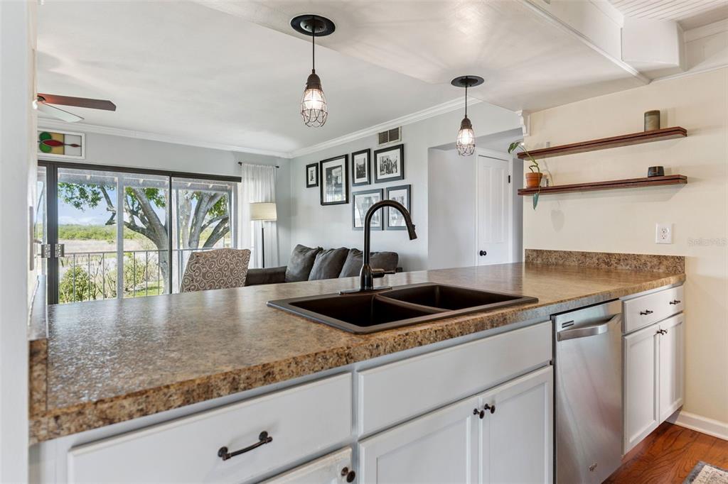 A kitchen island with a dark sink overlooks a living area with a sliding glass door — 210 LA CASA UNIT 210, LAKE WALES, FL