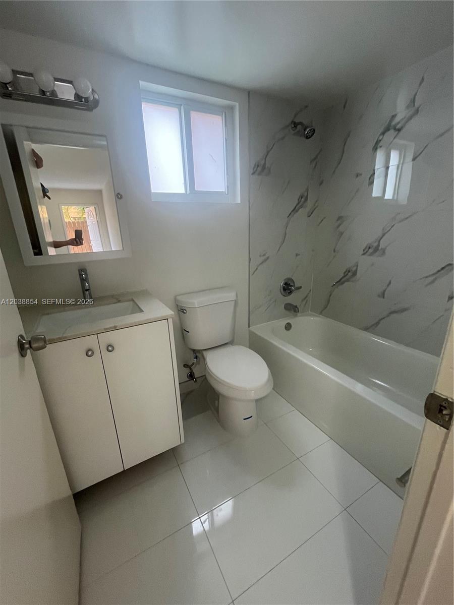 A bathroom features a white vanity, a toilet, and a bathtub with marble-patterned wall tiles — 1419 SW 22nd Ave, Miami FL 33145, MIAMI, FL