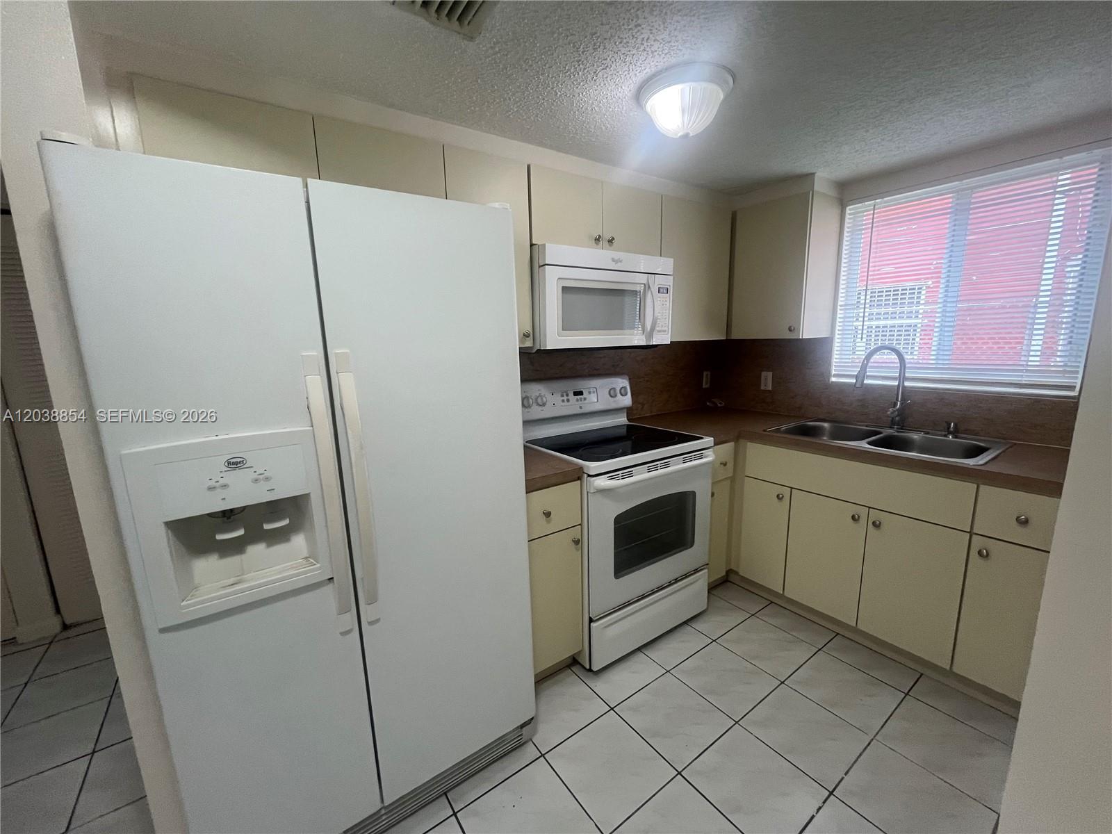 A kitchen features white appliances, light-colored cabinets, a double sink, and tiled flooring — 1419 SW 22nd Ave, Miami FL 33145, MIAMI, FL