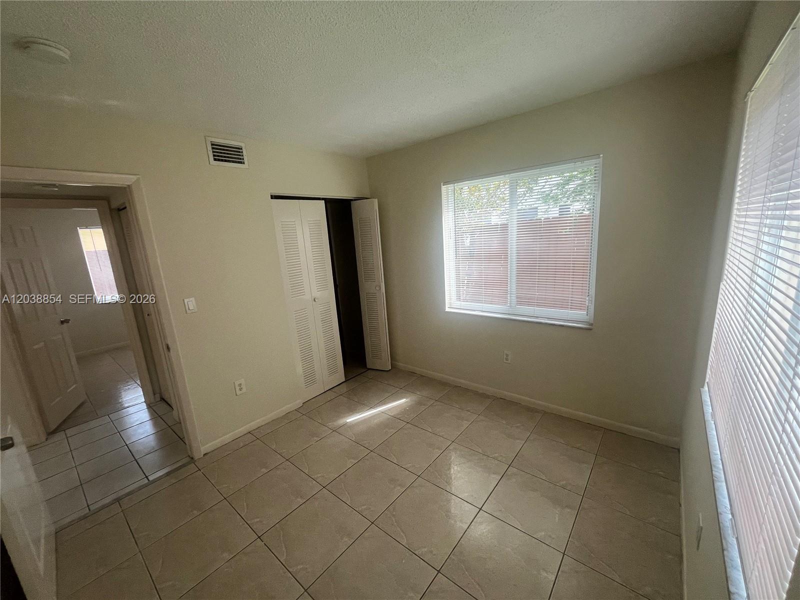An empty bedroom features light-colored tile flooring, a closet with louvered doors, and two windows — 1419 SW 22nd Ave, Miami FL 33145, MIAMI, FL