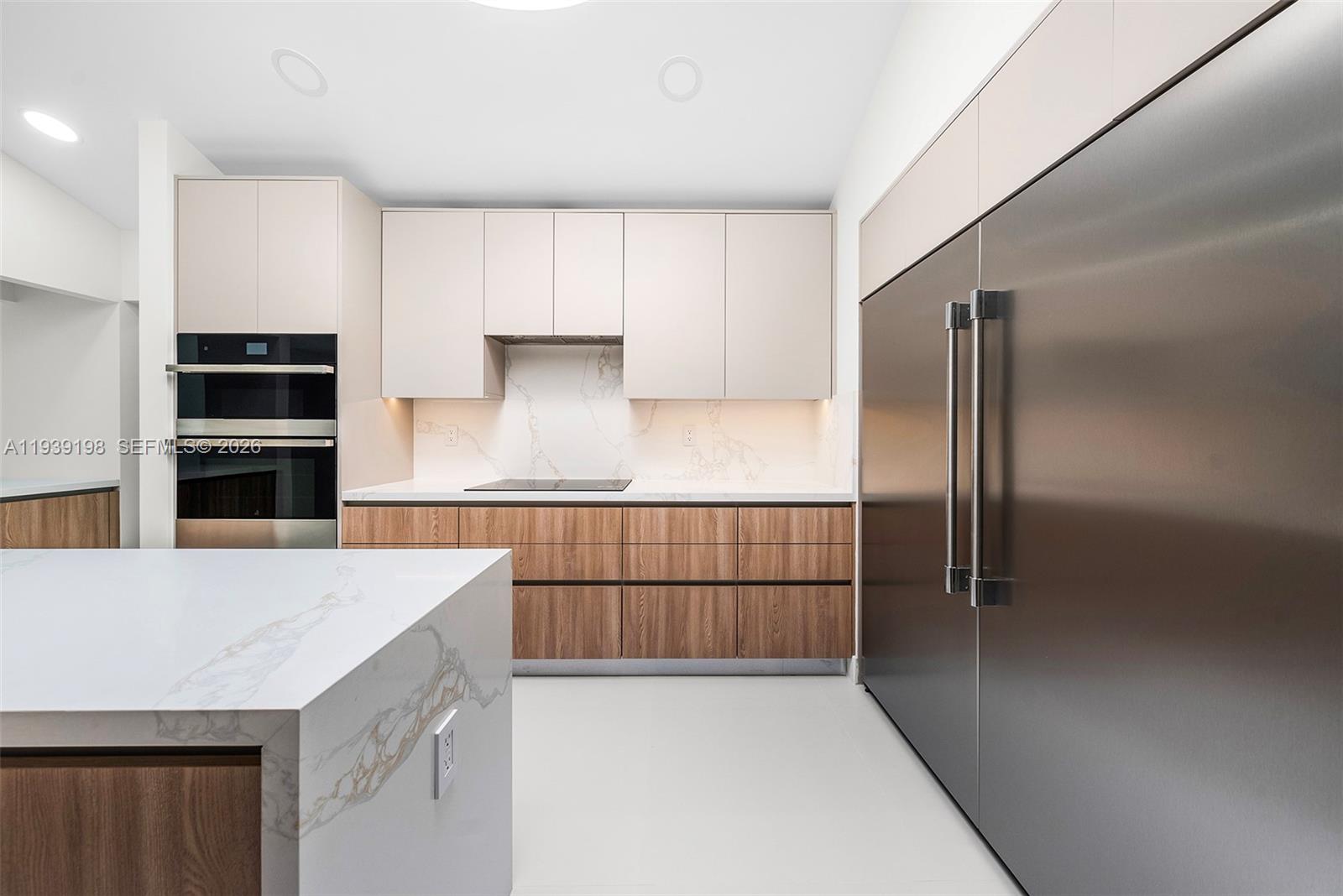 A modern kitchen features wood-grain lower cabinets, light upper cabinets, and a marble-topped island — 7540 Los Pinos Blvd, Coral Gables FL 33143, CORAL GABLES, FL