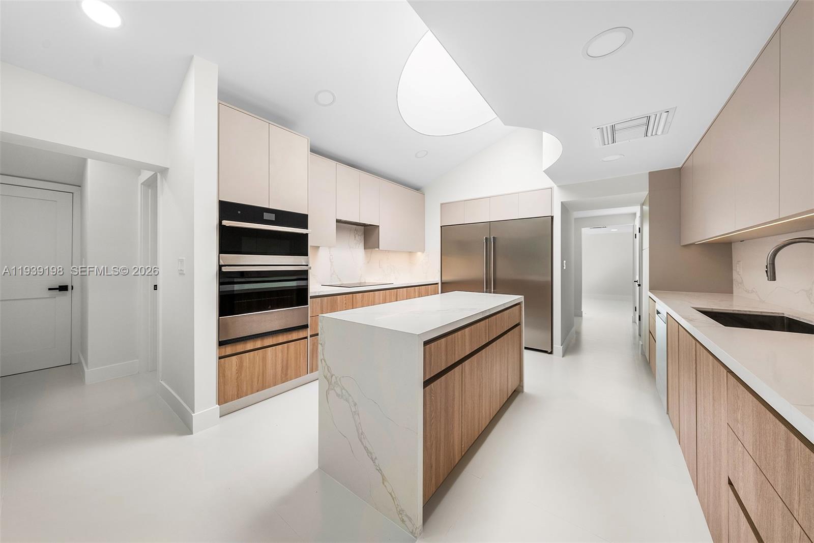 A modern kitchen features light wood cabinetry, a marble-topped island, and stainless steel appliances — 7540 Los Pinos Blvd, Coral Gables FL 33143, CORAL GABLES, FL