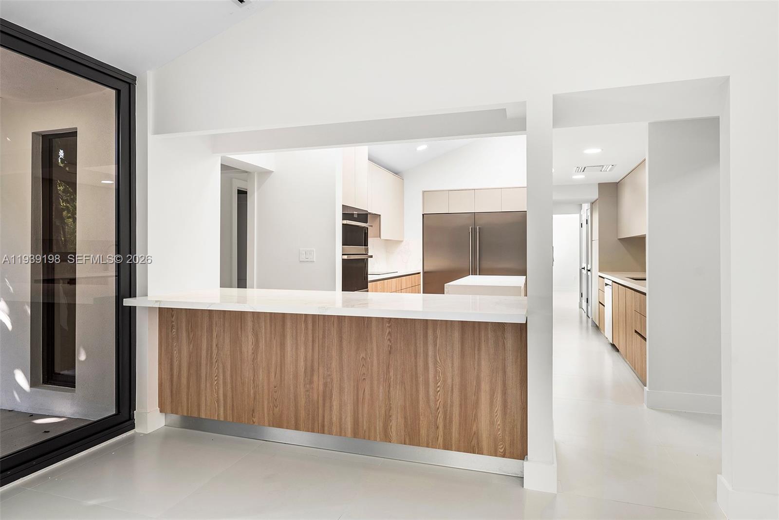 A modern kitchen features a wood-paneled breakfast bar, white countertops, and stainless steel appliances — 7540 Los Pinos Blvd, Coral Gables FL 33143, CORAL GABLES, FL