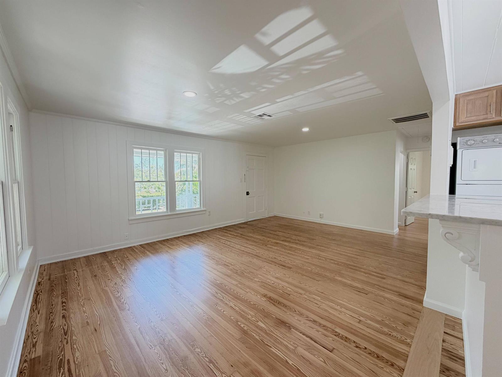 An empty living room with white paneled walls, hardwood floors, and a view of a porch — 1713 Florida Avenue # A2, West Palm Beach FL 33401, WEST PALM BEACH, FL