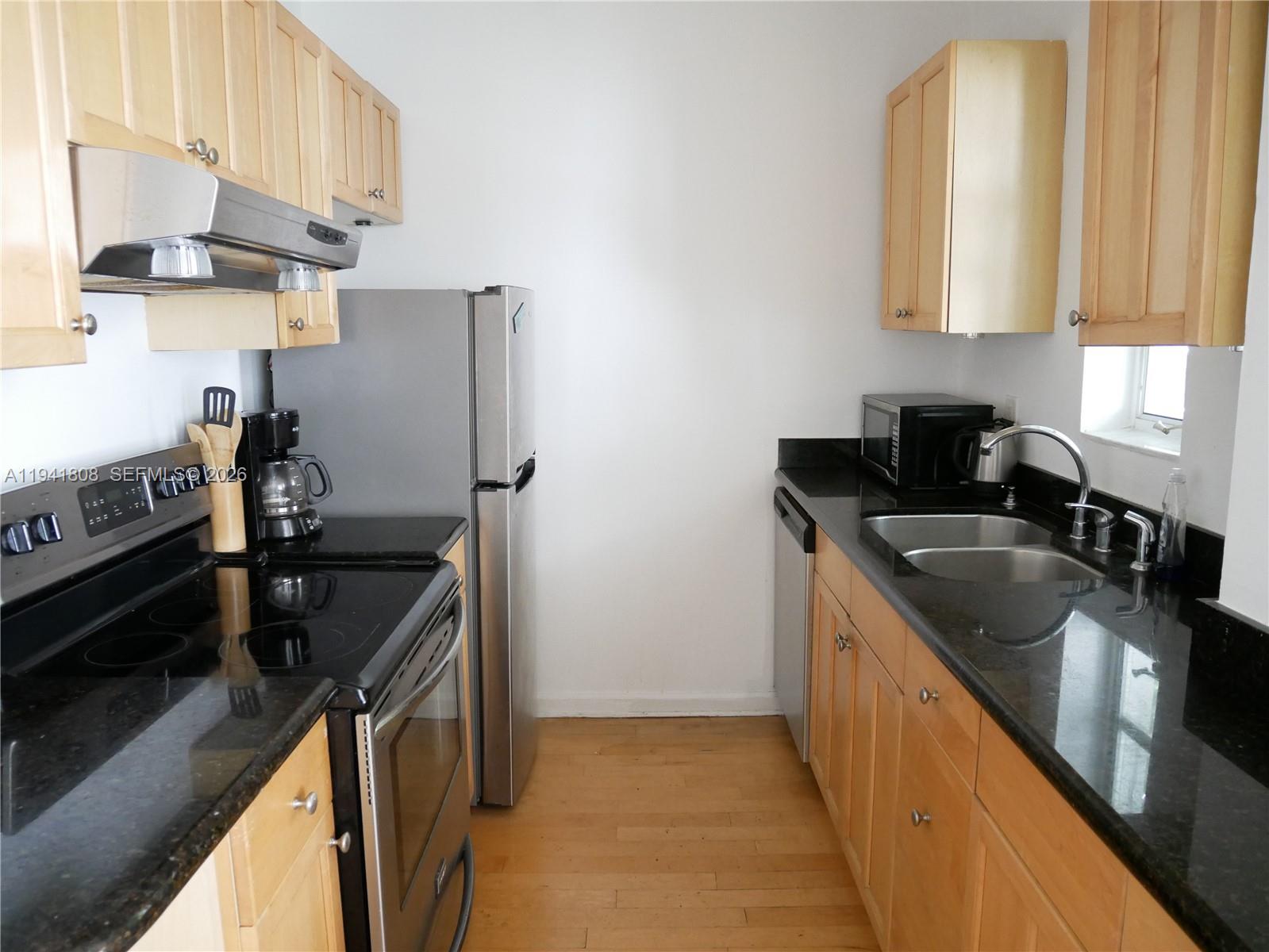 A galley kitchen features light wood cabinets, black granite countertops, and stainless steel appliances — 631 Euclid Ave # 7, Miami Beach FL 33139, MIAMI BEACH, FL