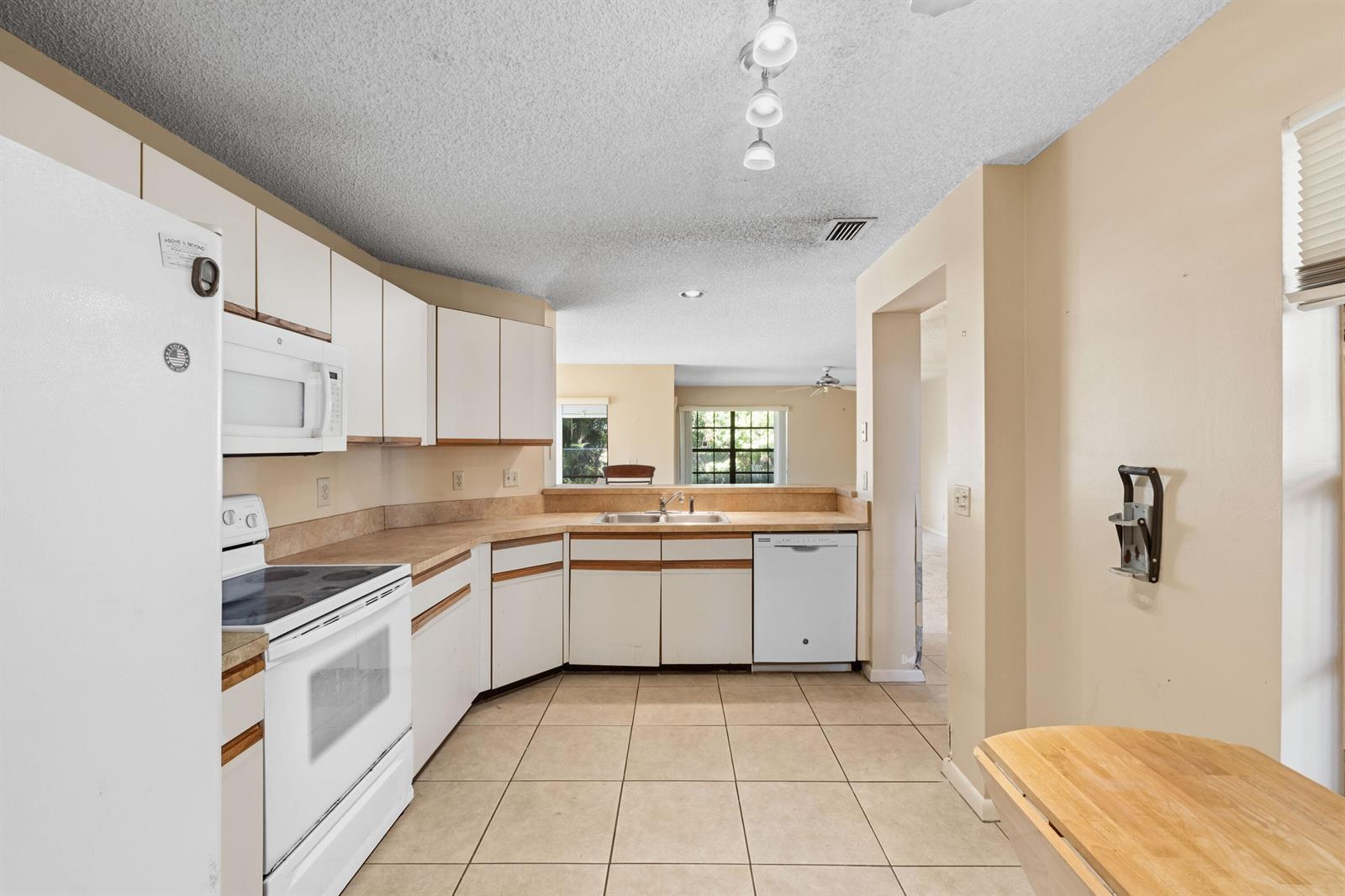A kitchen features white cabinets, light countertops, tile flooring, and a pass-through to another room — 3237 Perimeter Drive # 2512, FL 33467, FL