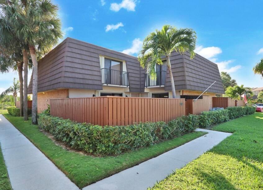 A two-story townhouse with a brown mansard roof, wooden privacy fence, and palm trees — 2117 21st Court, Jupiter FL 33477, JUPITER, FL