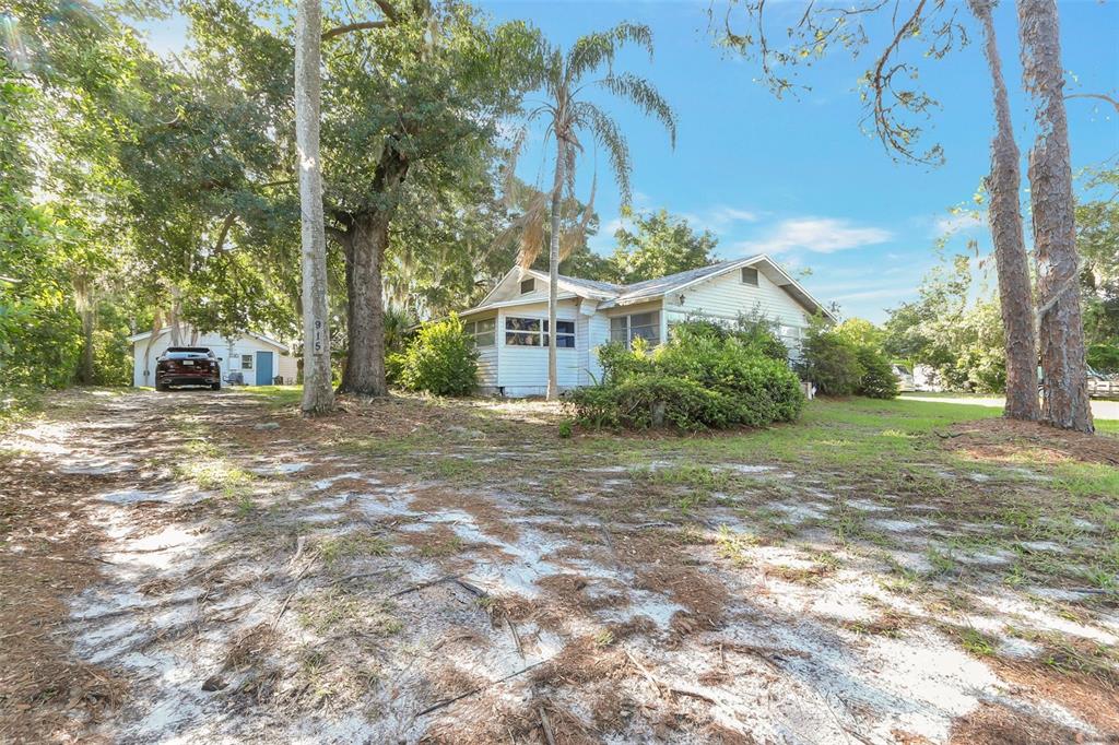 A single-story house with white siding sits on a sandy lot among many trees — 917 OXFORD STREET, LONGWOOD, FL