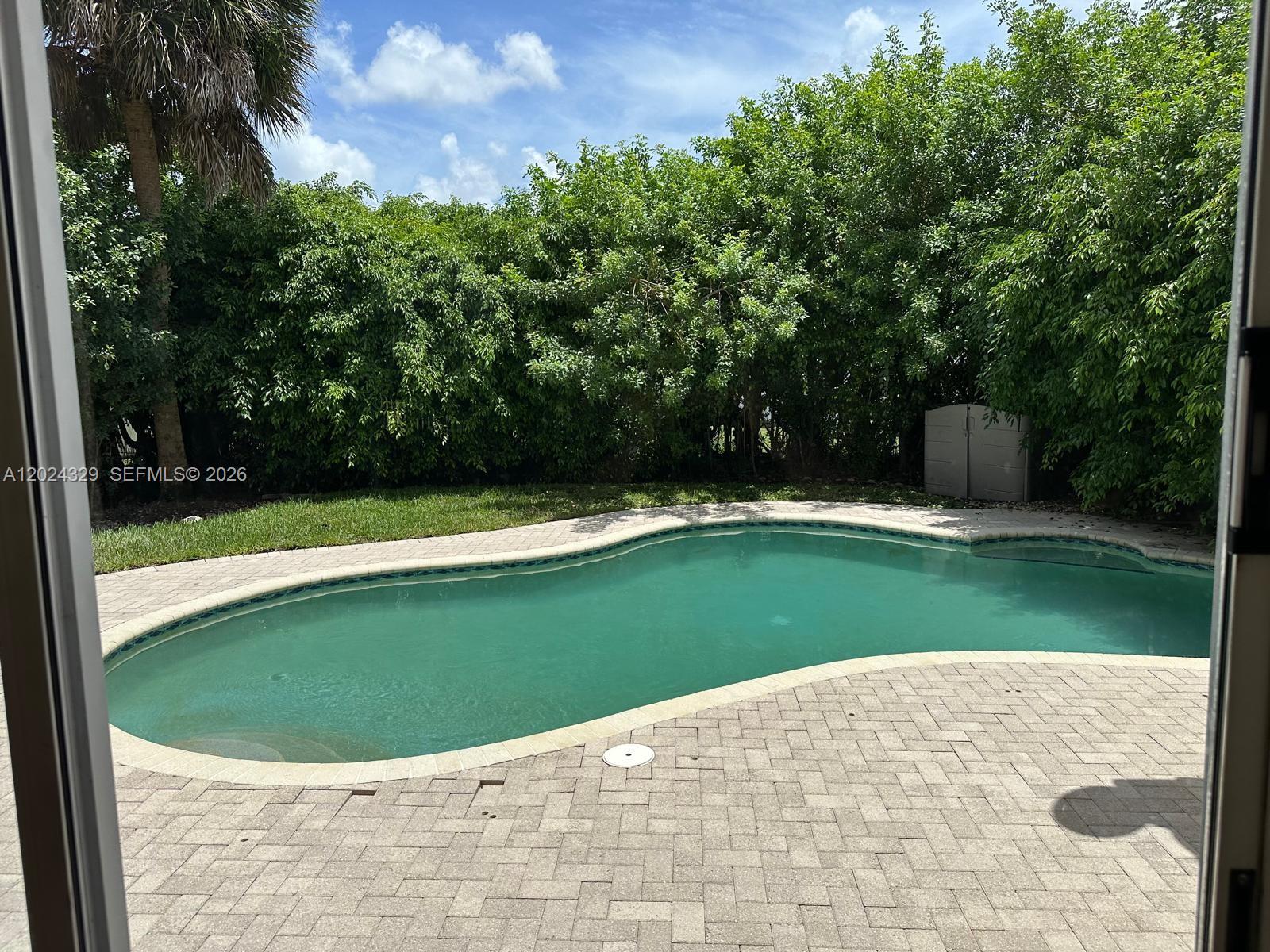 A kidney-shaped swimming pool sits on a paved patio surrounded by dense green trees — 11090 Baybreeze Way # 11090, Boca Raton FL 33428, BOCA RATON, FL