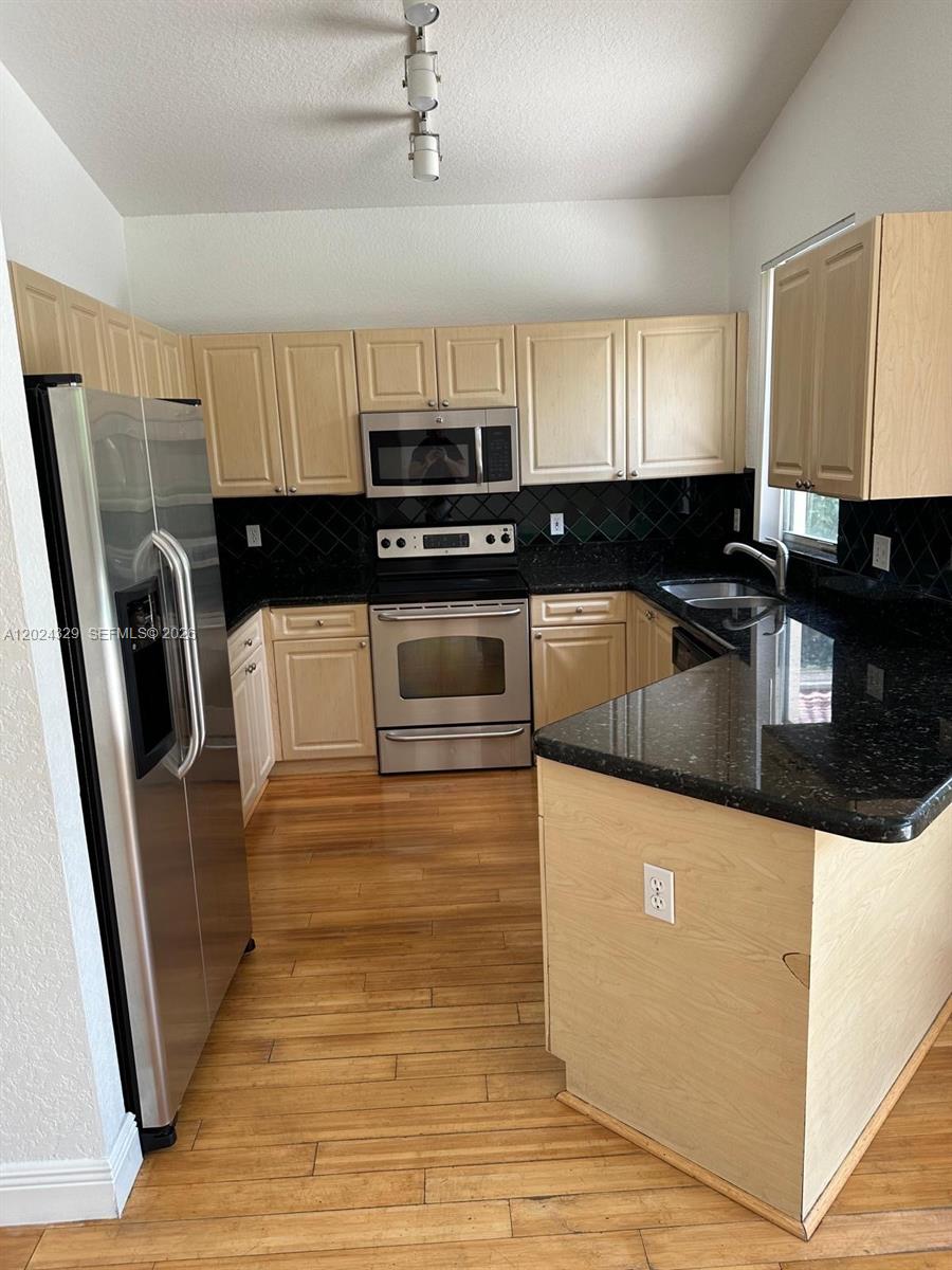 A kitchen features light wood cabinets, black countertops, stainless steel appliances, and hardwood flooring — 11090 Baybreeze Way # 11090, Boca Raton FL 33428, BOCA RATON, FL