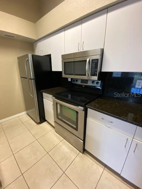 A kitchen features white cabinets, stainless steel appliances, and dark countertops over tiled flooring — 5028 PARK CENTRAL DRIVE UNIT 2128, ORLANDO, FL
