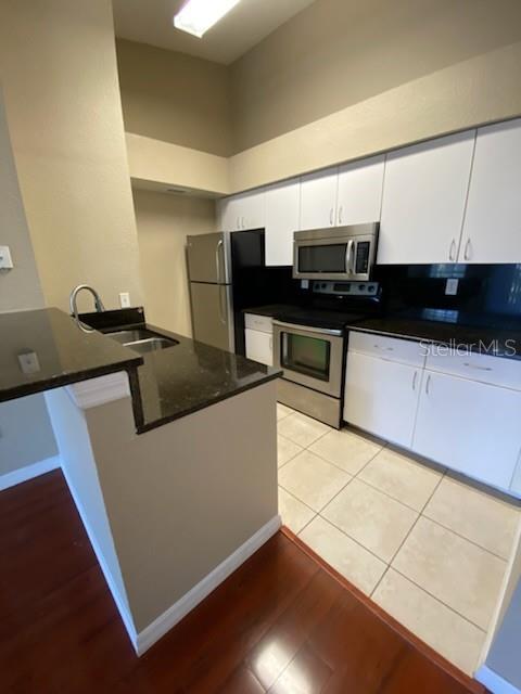 A kitchen features white cabinets, stainless steel appliances, dark countertops, and light tile flooring — 5028 PARK CENTRAL DRIVE UNIT 2128, ORLANDO, FL