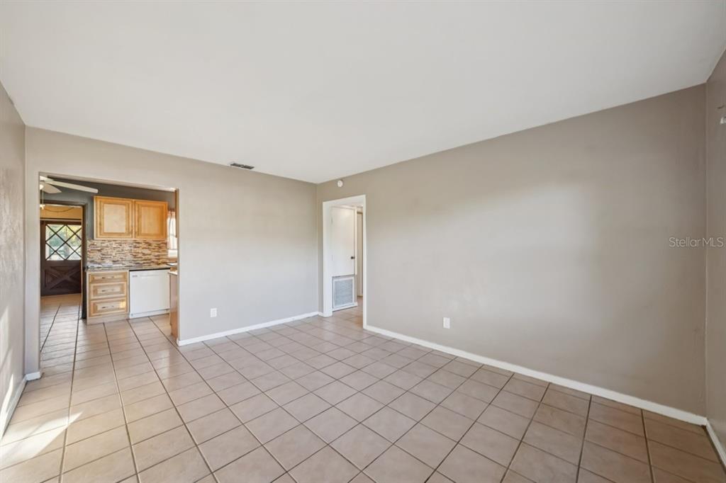 An empty room with beige walls and light-colored tile flooring leads into a kitchen — 603 OAK RIDGE DRIVE, BRANDON, FL