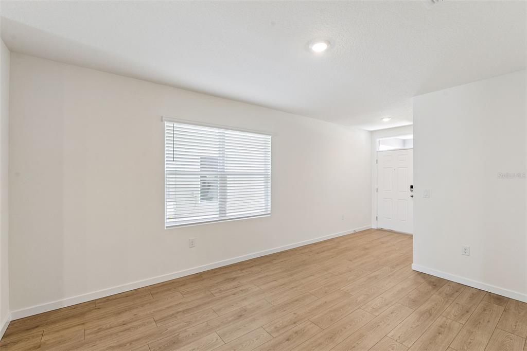 An empty room with light wood-look flooring, white walls, a window with blinds, and a door — 1349 CAMELLIA BLOOM LANE, SANFORD, FL