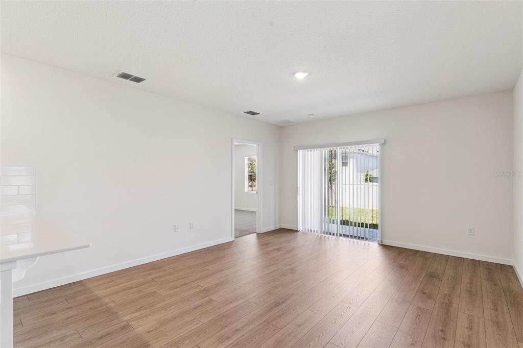An empty room with light wood-look flooring, white walls, and a sliding glass door — 1349 CAMELLIA BLOOM LANE, SANFORD, FL