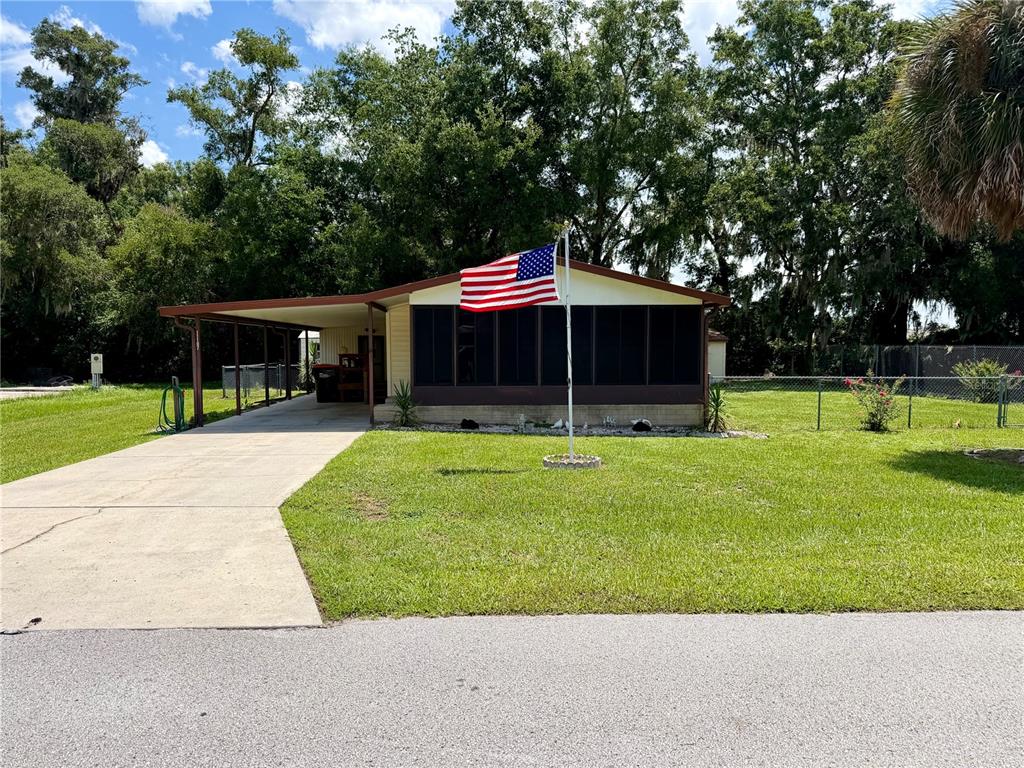 A single-story house with a screened porch, carport, and American flag in the front yard — 11107 SE 66TH TERRACE, BELLEVIEW, FL