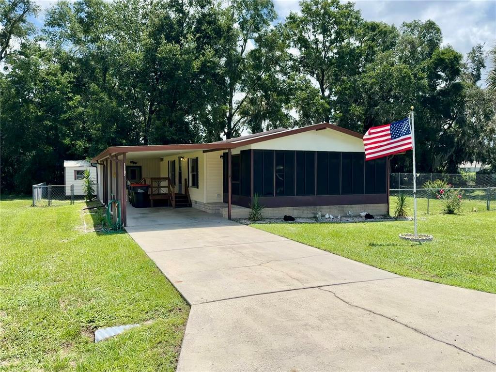 A single-story mobile home with a screened porch, carport, and American flag in the yard — 11107 SE 66TH TERRACE, BELLEVIEW, FL