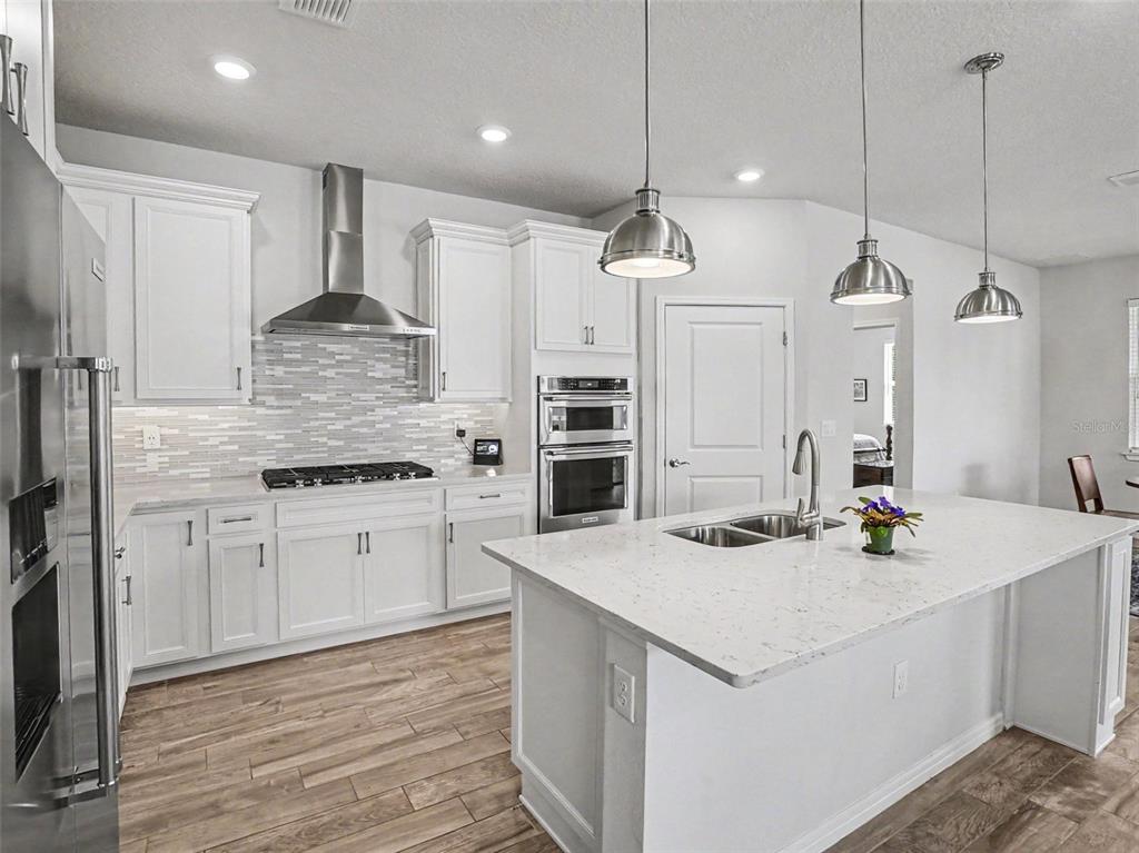 A modern kitchen features white cabinetry, stainless steel appliances, a large island, and wood flooring — 6261 CITRUS GROVE COURT, ST CLOUD, FL