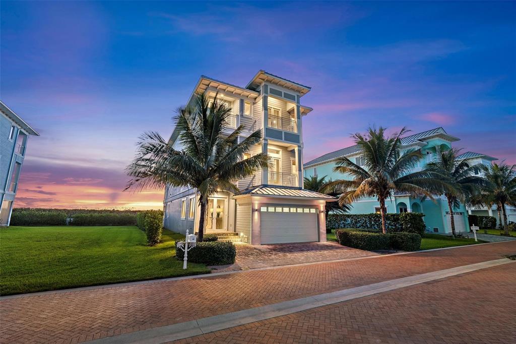 A three-story coastal home with a garage, palm trees, and a brick driveway at sunset — 4860 WATERSONG WAY, FORT PIERCE, FL