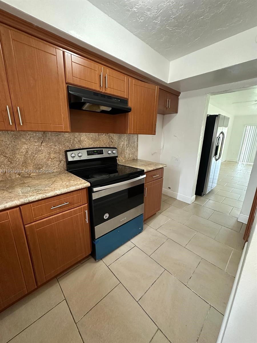 A kitchen features wood cabinets, a stainless steel stove, and beige tile flooring — 7344 SW 82nd St # C115, Miami FL 33143, MIAMI, FL