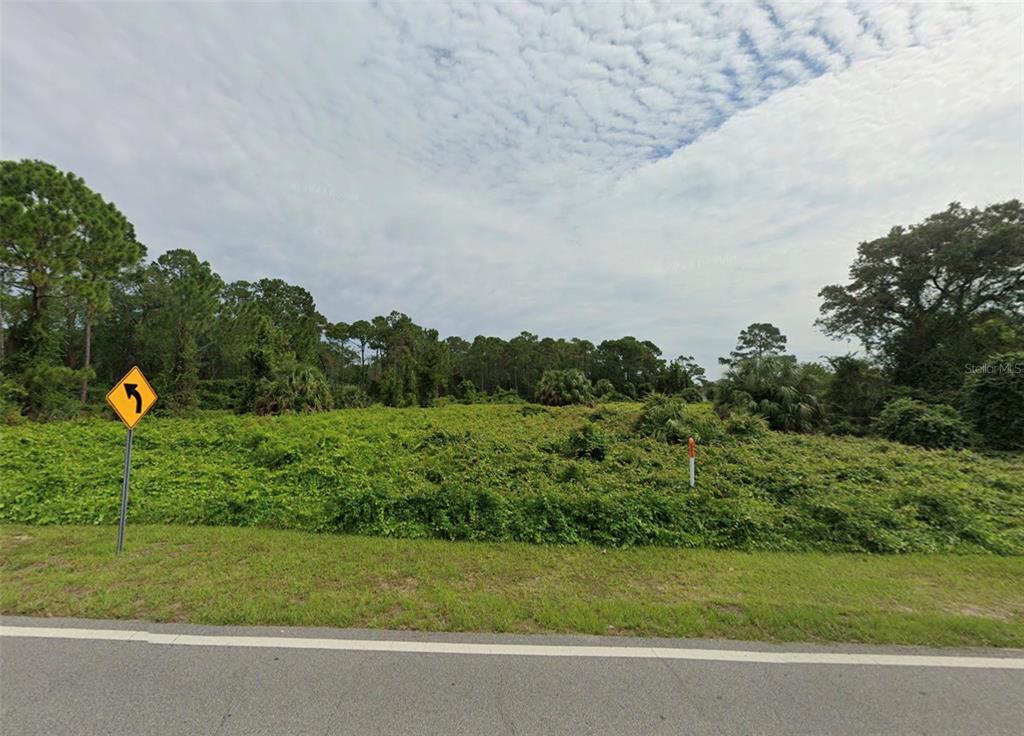 A vacant, overgrown lot sits beside a paved road with a yellow curve sign — 2700 CAPTAIN DRIVE, DELTONA, FL