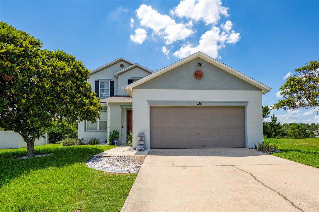 A two-story house with a beige stucco exterior, a two-car garage, and a front lawn — 130 BACOPA PASS, DAVENPORT, FL
