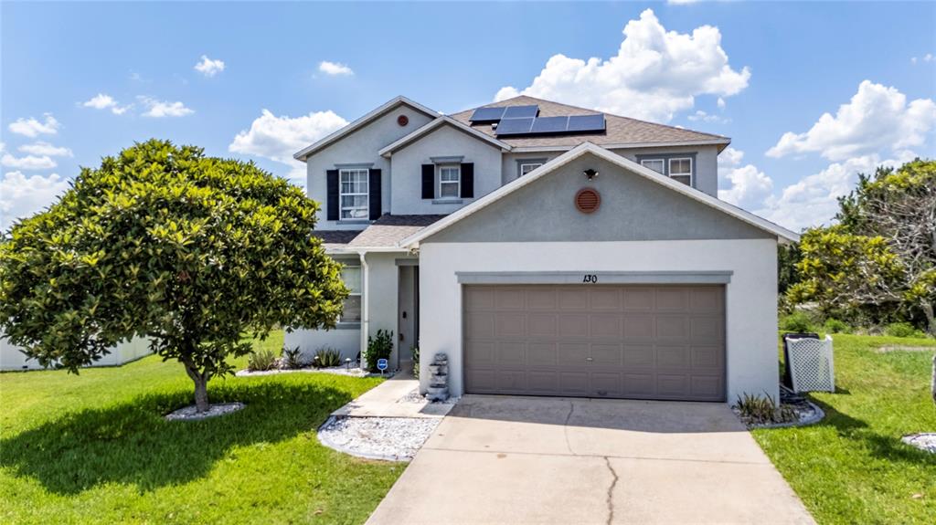 A two-story suburban house with a tan garage, light-colored stucco siding, and rooftop solar panels — 130 BACOPA PASS, DAVENPORT, FL