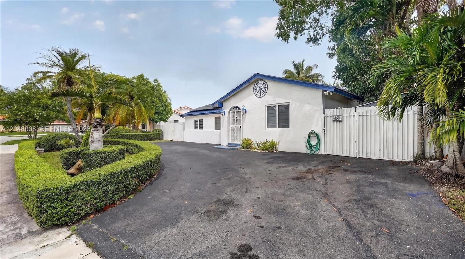 A white house with a blue roof and a large asphalt driveway sits behind hedges — 15022 SW 67th Ln, Miami FL 33193, MIAMI, FL
