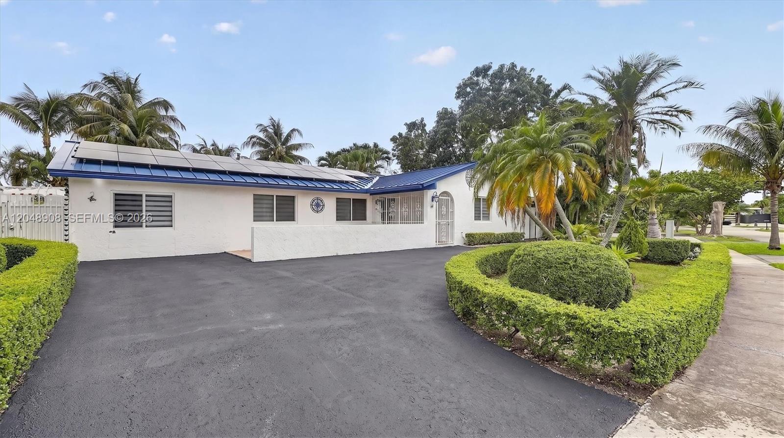 A white house with a blue metal roof and solar panels features a paved driveway — 15022 SW 67th Ln, Miami FL 33193, MIAMI, FL