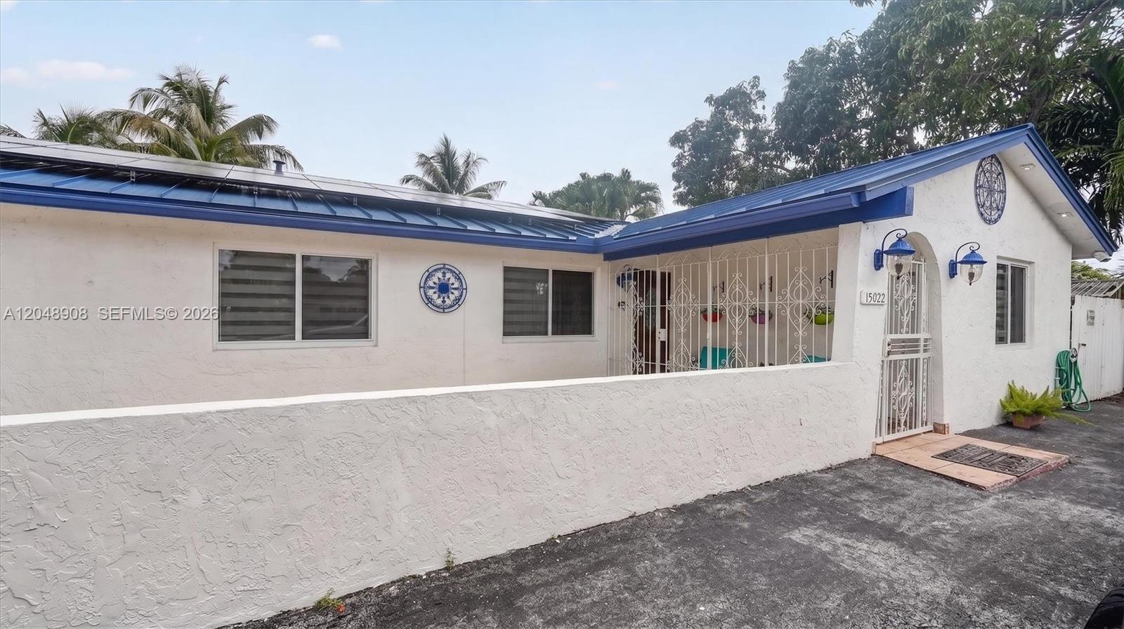 A white stucco house features a blue metal roof, solar panels, and a gated porch — 15022 SW 67th Ln, Miami FL 33193, MIAMI, FL
