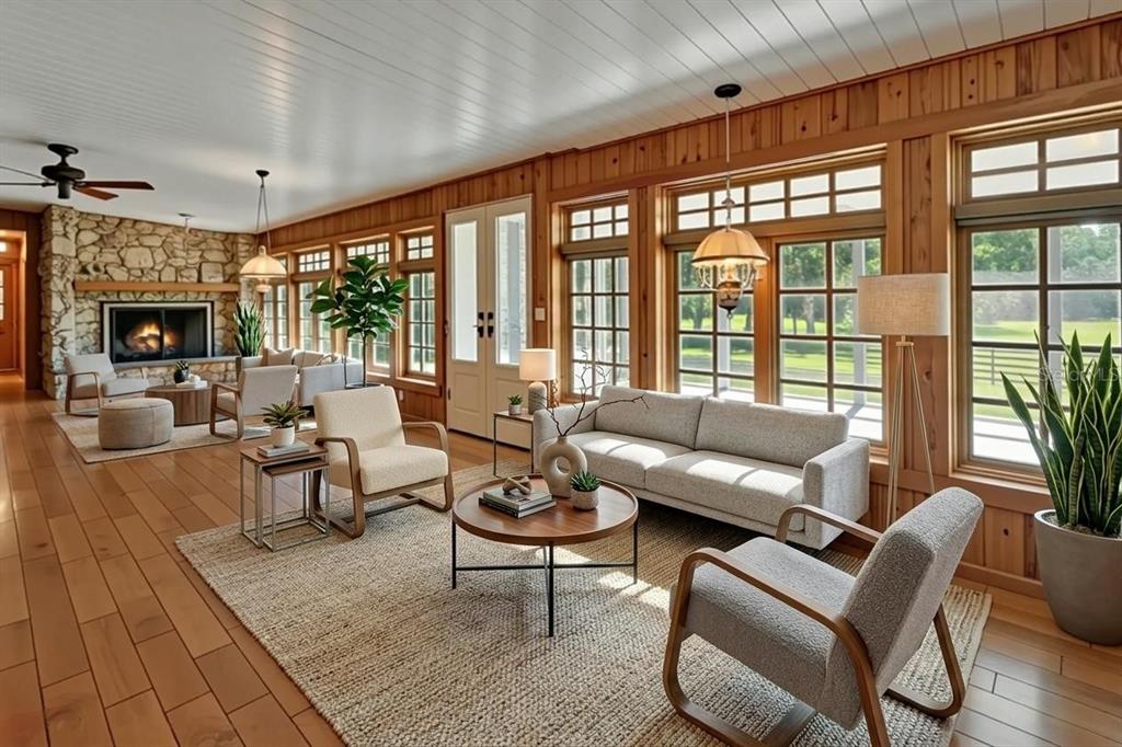 A spacious living room features wood-paneled walls, a stone fireplace, and large windows overlooking greenery — 900 E KICKLIGHTER (5 +- ACRES) ROAD, LAKE HELEN, FL