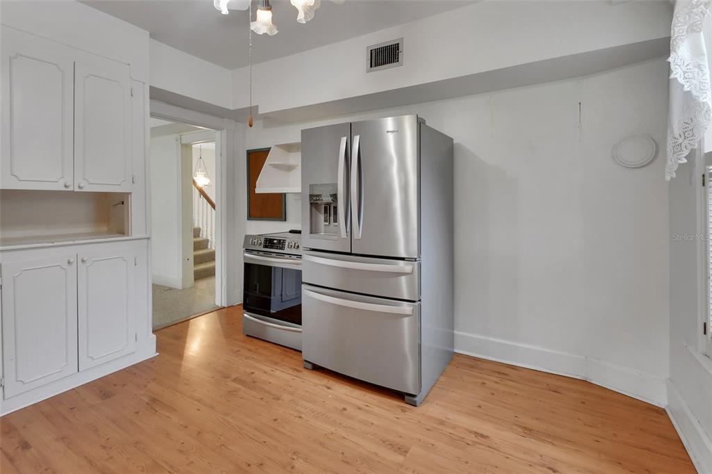 A kitchen features a stainless steel refrigerator, a range, white cabinetry, and wood flooring — 900 E KICKLIGHTER (5 +- ACRES) ROAD, LAKE HELEN, FL
