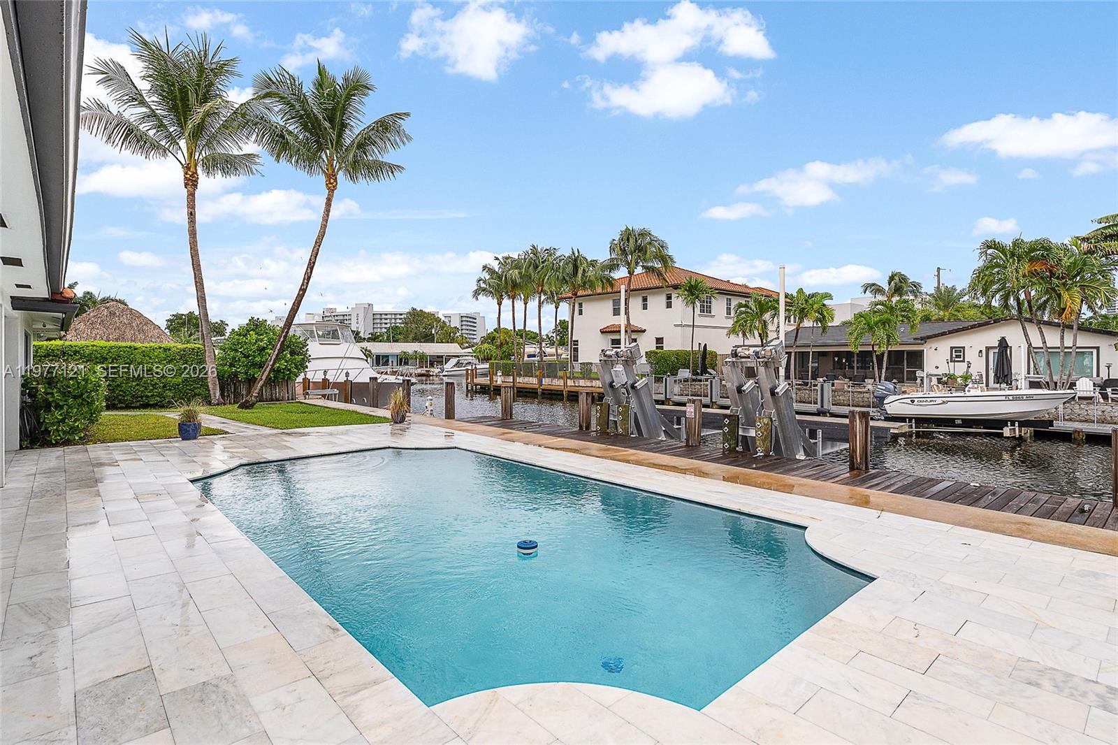 A swimming pool sits on a stone patio next to a canal with boat lifts — 1250 NE 27th Terrace, Pompano Beach FL 33062, POMPANO BEACH, FL