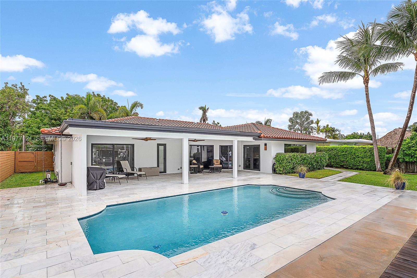 A backyard features a swimming pool, a covered patio, and palm trees under a blue sky — 1250 NE 27th Terrace, Pompano Beach FL 33062, POMPANO BEACH, FL
