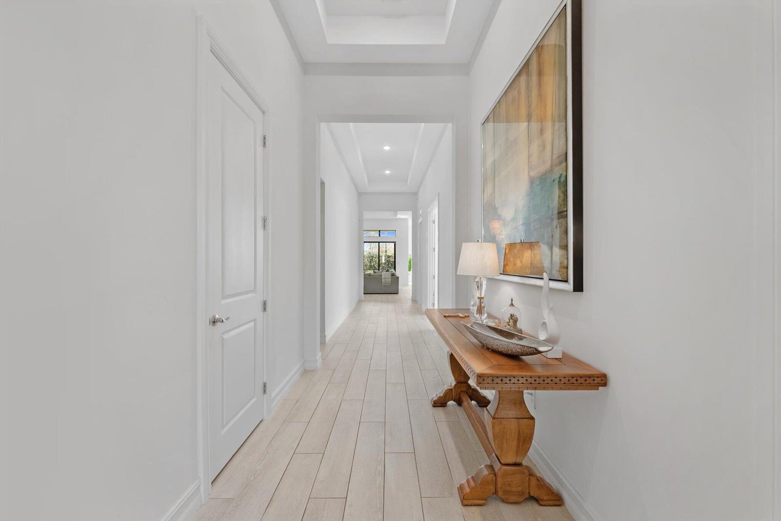A bright hallway features light wood-look flooring, a wooden console table, and a large painting — 11770 Leon Circle S, Parkland FL 33076, PARKLAND, FL