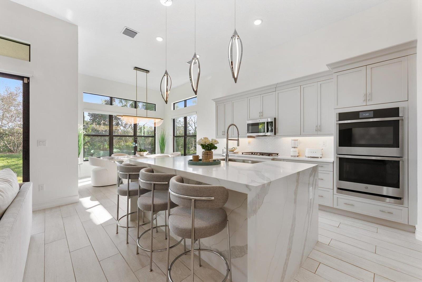 A modern kitchen features a marble waterfall island, gray cabinetry, and stainless steel appliances — 11770 Leon Circle S, Parkland FL 33076, PARKLAND, FL