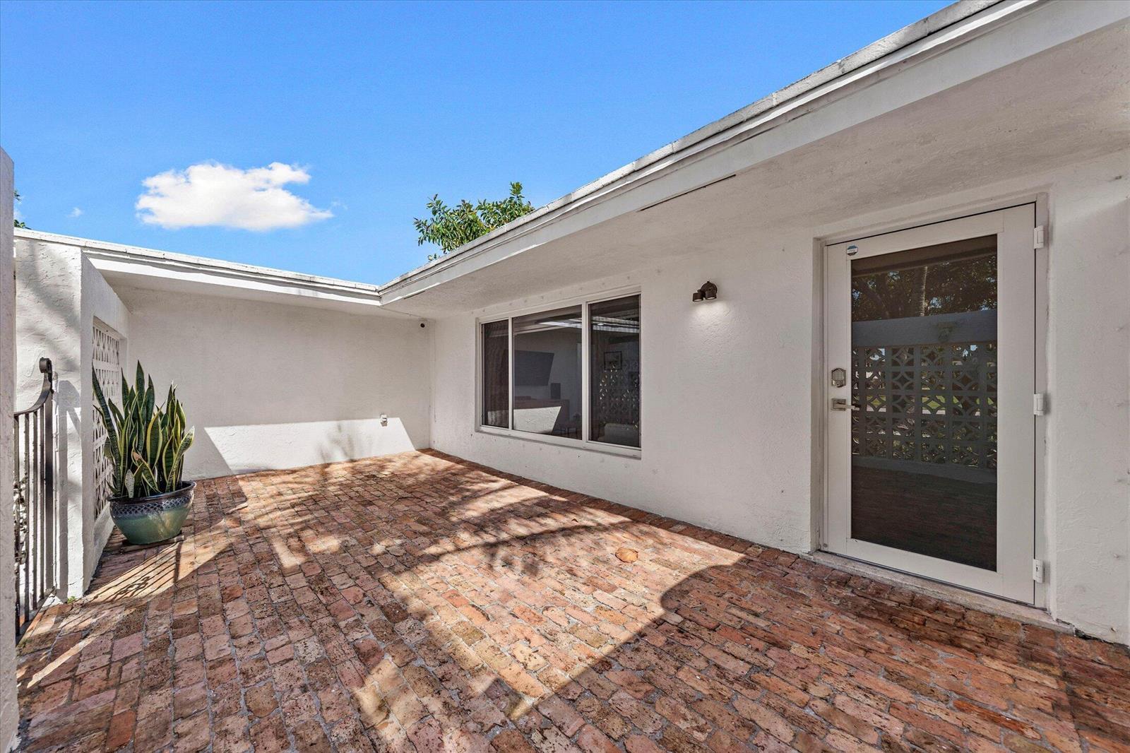 A brick patio sits outside a white house with a glass door and large window — 421 SW 18th Street, Pompano Beach FL 33060, POMPANO BEACH, FL