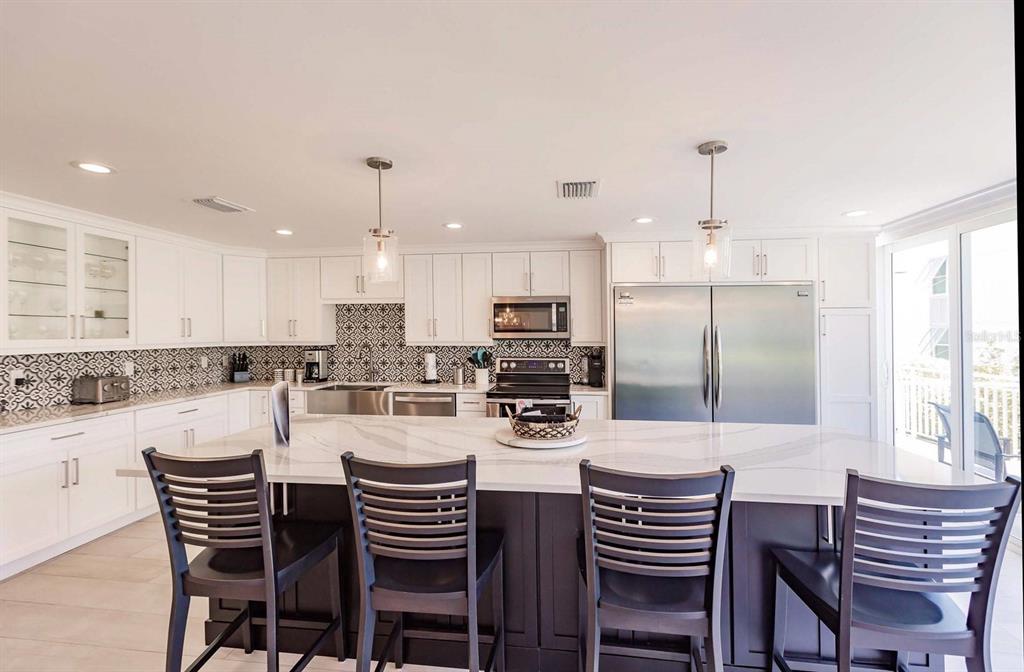 A modern kitchen features white cabinetry, a large marble-topped island, and a patterned tile backsplash — 1125 W PEPPERTREE DRIVE UNIT 102, SARASOTA, FL