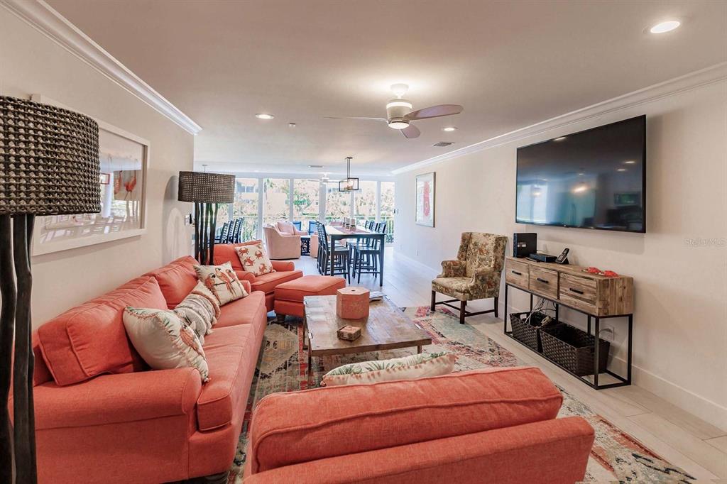 A living room features a coral sofa, a wooden coffee table, and a wall-mounted television — 1125 W PEPPERTREE DRIVE UNIT 102, SARASOTA, FL