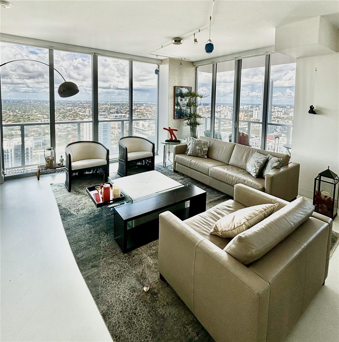 A modern living room features floor-to-ceiling windows with city views and neutral leather furniture — 79 SW 12th St, Miami FL 33130, MIAMI, FL