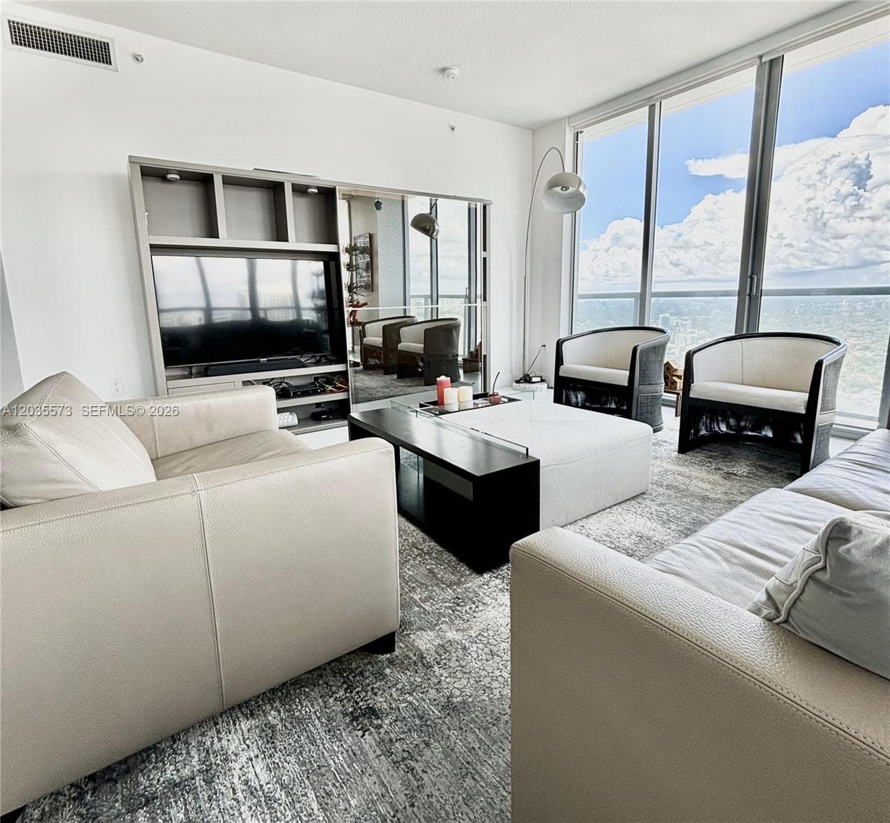 A modern living room features light-colored leather sofas, a central ottoman, and floor-to-ceiling windows — 79 SW 12th St, Miami FL 33130, MIAMI, FL