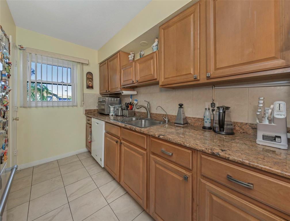 A kitchen features wood cabinets, granite countertops, a stainless steel sink, and tile flooring — 6976 SUNSET DRIVE S UNIT 6976, ST PETERSBURG, FL